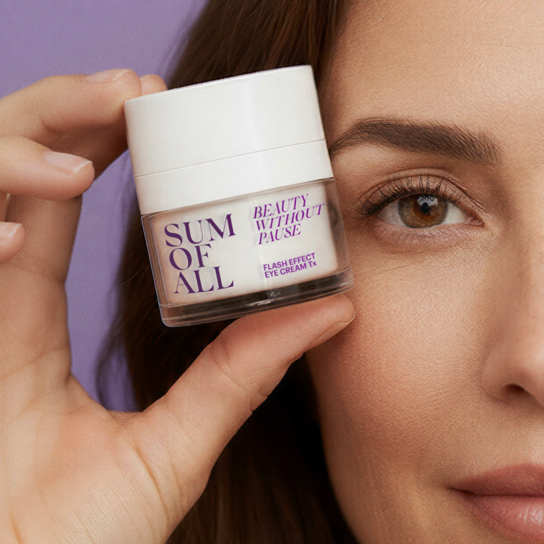 Person holding a jar of 'Sum of All' flash effect eye cream tx close to their face.