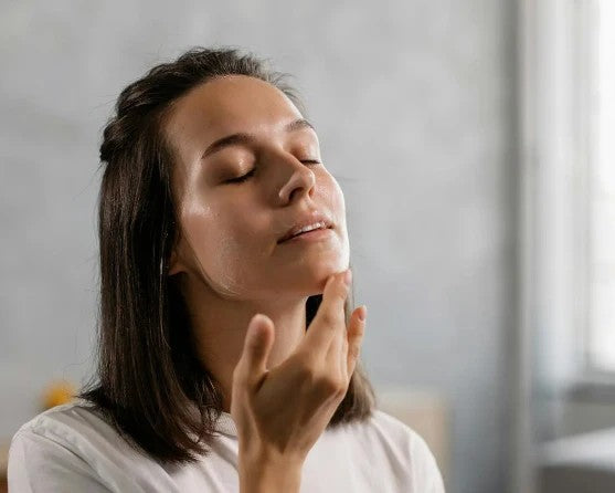 Woman applying a facial product with a neutral background
